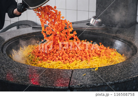 male chef roasts carrots in cauldron to cook traditional Uzbek pilaf in kitchen at restaurant in Uzbekistan 116508758