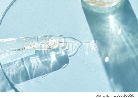 Serum gel texture swatch. Transparent drop golden sparkles. Blue background 116510059