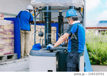 トラックにフォークリフトで荷物を積むヘルメット姿の作業員 116510701