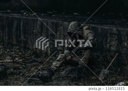 A man in dark green camouflage and a gas mask sits among the ruins of the city. A man in dark green camouflage and a gas mask sits among the ruins of the city. 116512815