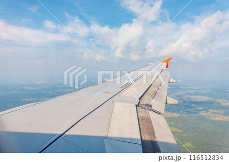 View of airplane wing, blue skies and green land during landing. Airplane window view. 116512834