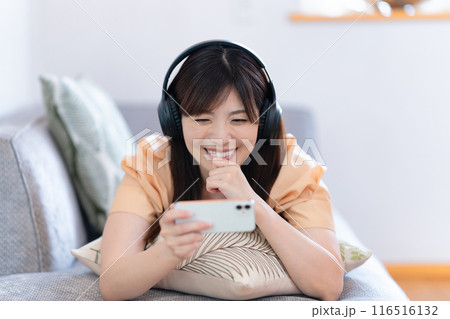 ソファに寝転んでスマホ動画を観る女性 116516132