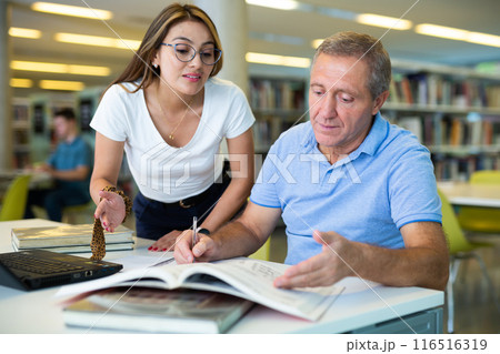 Young female Latina tutor teaching a mature caucasian elder Young female Latina tutor teaching a mature caucasian elder 116516319