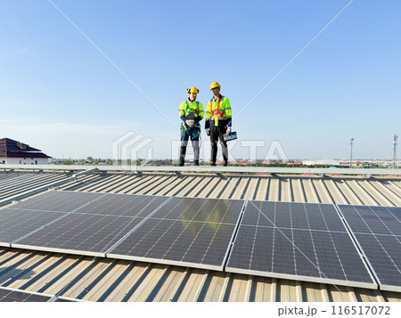 Professional electric engineers survey and inspect solar panels installation on the factory metal sheet roof top, electric engineer team inspecting and check solar cell system. 116517072