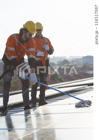 Professional electrical engineers working on the residential rooftop to clean up the dusty solar panels. Professional electrical engineers working on the residential rooftop to clean up the dusty solar panels. 116517087