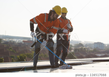 Professional electrical engineers working on the residential rooftop to clean up the dusty solar panels. Professional electrical engineers working on the residential rooftop to clean up the dusty solar panels. 116517088