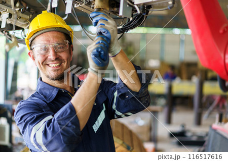 Professional caucasian white ethnicity male technician operating the heavy duty machine in the lathing factory. Technician in safety and helmet suit controlling a machine in factory. 116517616