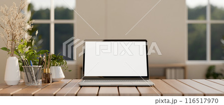 A laptop computer with a white-screen mockup on a wooden table in a contemporary minimalist room. 116517970