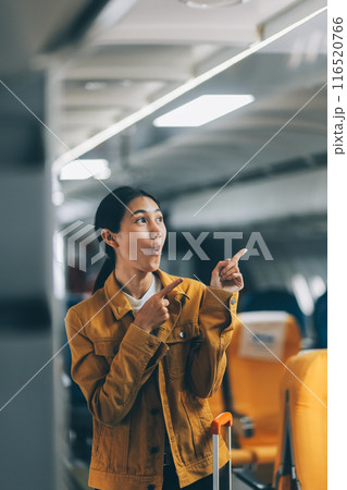 Young Female Tourist with Luggage Walking Through Airplane Cabin Ready for Travel Adventure Young Female Tourist with Luggage Walking Through Airplane Cabin Ready for Travel Adventure 116520766