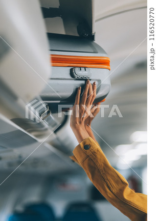 Young Female Tourist Storing Luggage in Overhead Compartment on Airplane During Travel 116520770