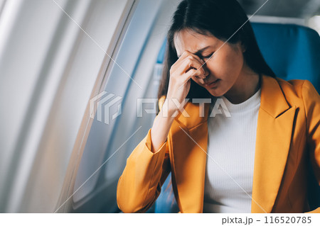 Young asian chinese airplane passenger woman experiencing discomfort, Airplane headache. Worried female passenger holding head, feeling unwell Anxiety and fear in the skies. Stressful travel moments. 116520785