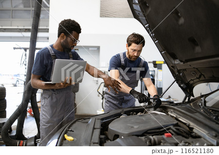 Two mechanics working on car engine in garage 116521180