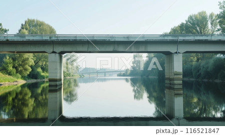 a concrete bridge crossing over a calm river. The sky is bright blue. 116521847