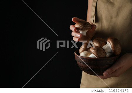 Champignon mushrooms in bowl in female hands on black background, space for text 116524172