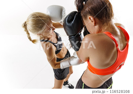 Close-up shot of female boxers in the heat of the battle, exchanging punches and focusing on defense isolated on white background Close-up shot of female boxers in the heat of the battle, exchanging punches and focusing on defense isolated on white background 116528108