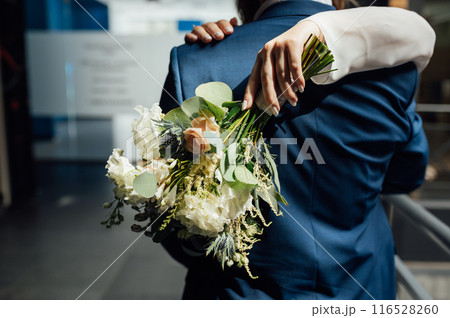 The bride and groom are hugging. The bride hugs the groom's neck and holds her bouquet of flowers 116528260