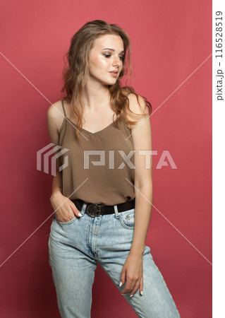 Stylish young adult woman in silk top wearing light jacket standing against red studio wall Stylish young adult woman in silk top wearing light jacket standing against red studio wall 116528519