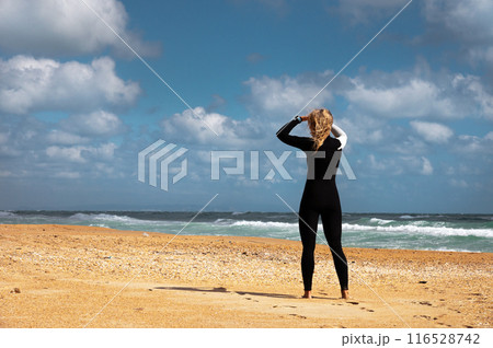 young woman in a wetsuit stands on the beach on...の写真素材 [116528742] - PIXTA