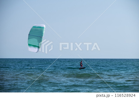 Young Caucasian woman athlete ride on a hydrofoil board with a kite in the open ocean. Hydrofoil is a new direction in kitesurfing Young Caucasian woman athlete ride on a hydrofoil board with a kite in the open ocean. Hydrofoil is a new direction in kitesurfing 116528924