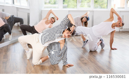 Man and his students perform hip hop dance on one bent leg, movement in horizontal plane near floor 116530081