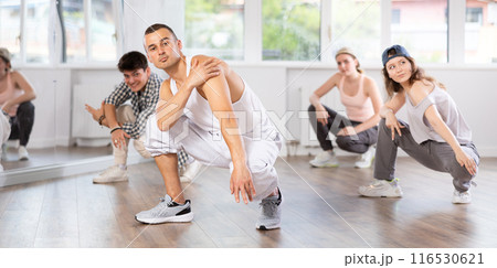 Young guy performing sitting pose of breakdance in training hall Young guy performing sitting pose of breakdance in training hall 116530621
