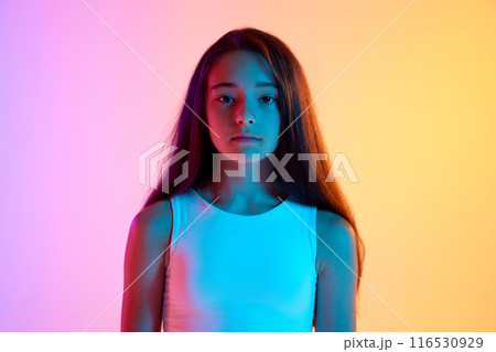 Portrait of beautiful young girl with long brown hair posing with calm expression against gradient pink yellow background in neon light 116530929