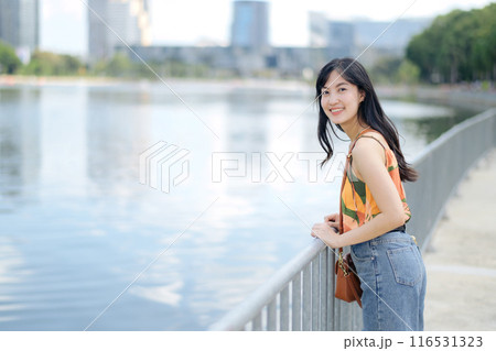 Urban charm meets natural bliss as a stylish woman in orange shirt enjoys a sunny day by the lake. Urban charm meets natural bliss as a stylish woman in orange shirt enjoys a sunny day by the lake. 116531323