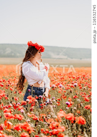 Happy woman in a poppy field in a white shirt and denim skirt with a wreath of poppies on her head posing and enjoying the poppy field. 116532745