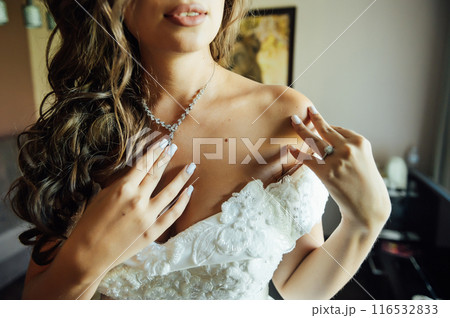 Wedding. Jewelry. The bride in a white dress putting on a necklace around his neck Wedding. Jewelry. The bride in a white dress putting on a necklace around his neck 116532833