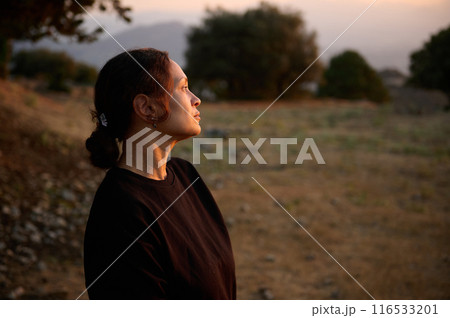 Woman admiring sunset in scenic countryside landscape, reflecting and appreciating nature 116533201