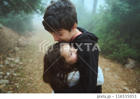 Tender moment of siblings hugging outdoors on a foggy day in the forest 116535053