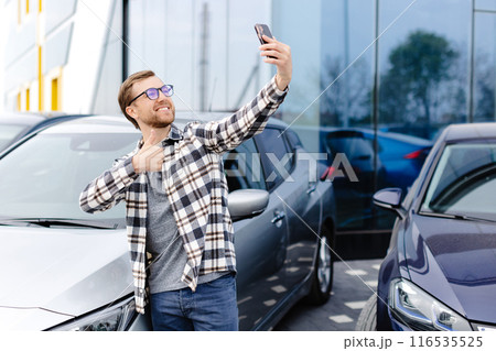 Happy man taking selfie through smart phone after purchasing new car. The man showing the purchased car via video link over the phone 116535525