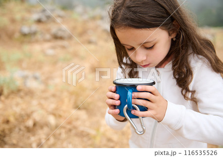 Young girl holding a blue mug with carabiner in a natural setting wearing a white jacket 116535526