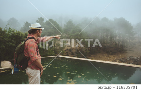 Man pointing towards forest in misty mountain landscape during hiking trip 116535701