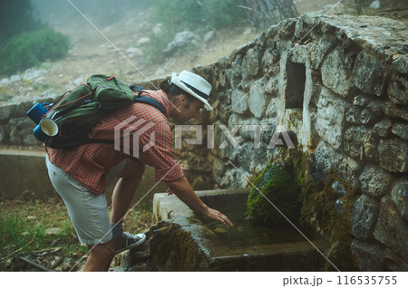 Man refilling water bottle at stone well during a misty mountain hike Man refilling water bottle at stone well during a misty mountain hike 116535755