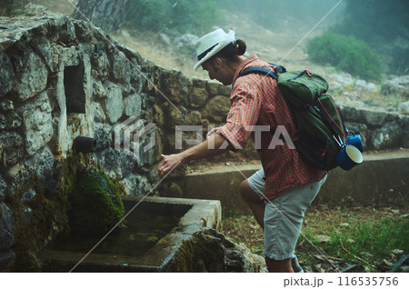 Hiker replenishing water supply at an old stone fountain in a misty forest 116535756