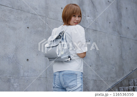防災用リュックサックを背負った女性の後ろ姿。コンクリート建物の背景 116536350