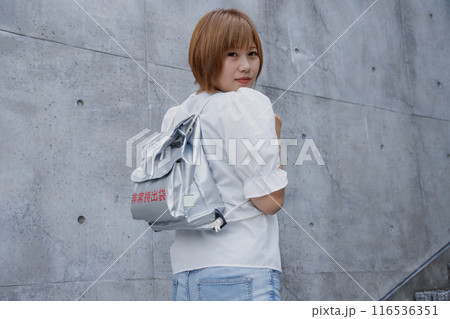 防災用リュックサックを背負った女性の後ろ姿。コンクリート建物の背景 防災用リュックサックを背負った女性の後ろ姿。コンクリート建物の背景 116536351