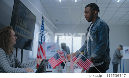 Female polling officer consults male voter, gives ballot for voting Female polling officer consults male voter, gives ballot for voting 116536547