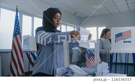 Muslim woman in hijab puts ballot paper in box at polling station 116536557