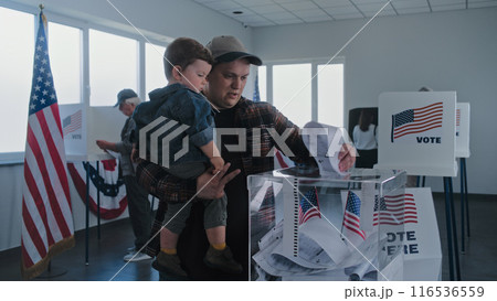African American man and Caucasian man with child put ballots in box 116536559