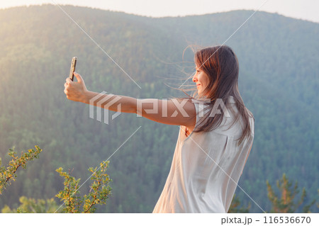 Woman taking a selfie in a mountainous landscape at sunset, enjoying the serene nature Woman taking a selfie in a mountainous landscape at sunset, enjoying the serene nature 116536670