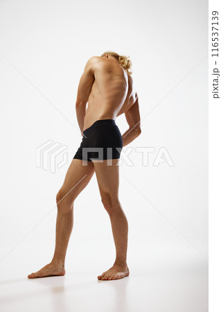 Full length photo of young, shirtless man posing in black underwear showing his muscular body against white studio background. 116537139