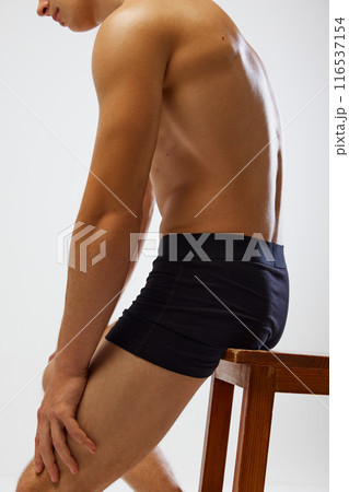 Close up photo of man's toned, tanned muscular upper body, arms against white studio background. Model sitting on wooden stool. Close up photo of man's toned, tanned muscular upper body, arms against white studio background. Model sitting on wooden stool. 116537154