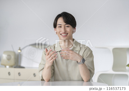 カメラ目線で話すイヤホンをした20代の男性 116537173