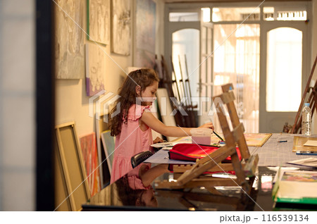 Young girl painting during art class in a workshop with colorful paintings around her 116539134