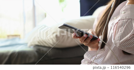Female sitting on couch with smartphone and listening music Female sitting on couch with smartphone and listening music 116540296