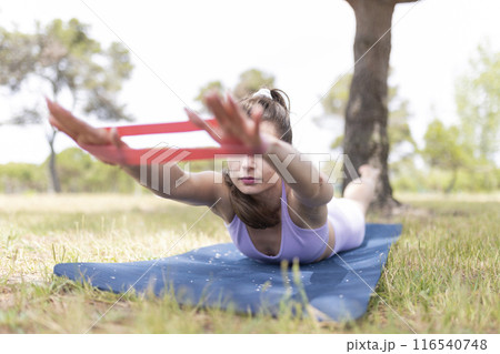 A Young Woman Utilizing a Resistance Band for Her Workout Routine in the Outdoors of a Park A Young Woman Utilizing a Resistance Band for Her Workout Routine in the Outdoors of a Park 116540748