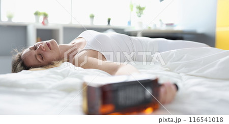 Drunk woman sleeping in bed and holding bottle of whisky 116541018