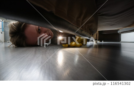 Woman using flashlight to look for something under bed 116541302